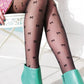 Woman wearing TABBISOCKS brand Ribbon Sheer Tights black pantyhose with black ribbon embroidery throughout, pink dress and emerald green leather short boots