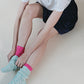 Woman sitting and double wearing the pink color of TABBISOCKS brand Washable 100% Finest Silk Toe Liner Socks with light blue socks