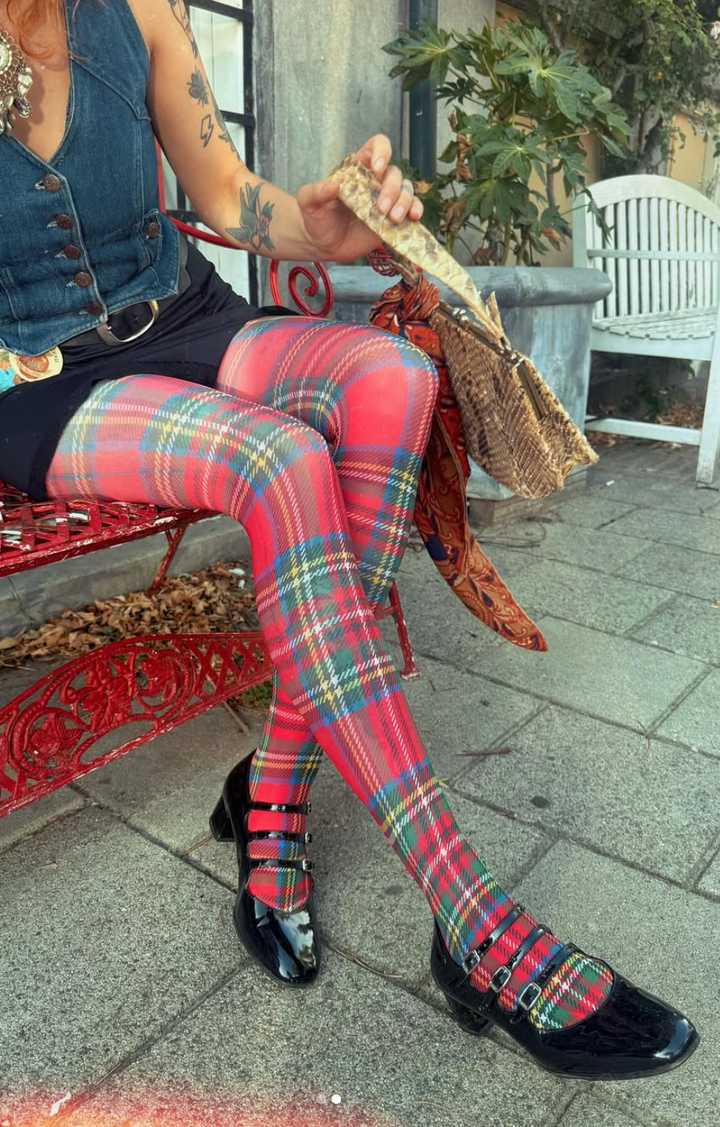 Person wearing red plaid tights with black shoes sitting on a red bench.