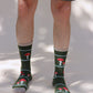 Male lower body in Grey half pants wearing TABBISOCKS brand Replant Pairs Mushroom Socks in green Olive color with red mushroom design with white dots throughout and ivory point color at the toe and mouth of the socks