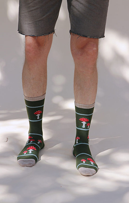 Male lower body in Grey half pants wearing TABBISOCKS brand Replant Pairs Mushroom Socks in green Olive color with red mushroom design with white dots throughout and ivory point color at the toe and mouth of the socks