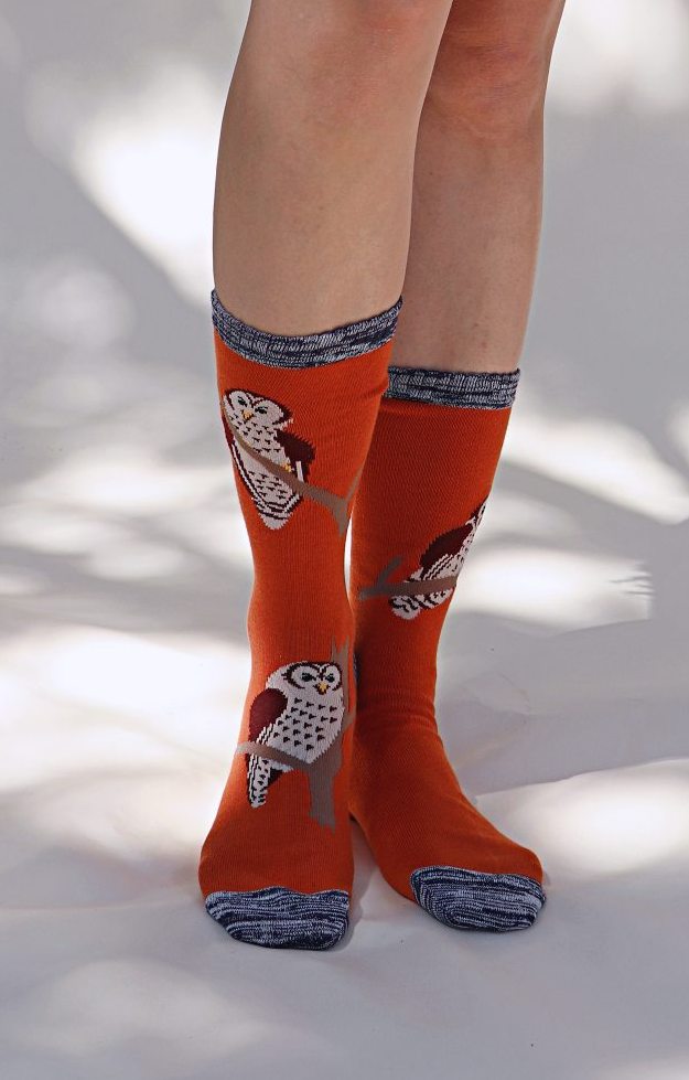 Female leg wearing TABBISOCKS brand Replant Pairs Owl Socks in orange pumpkin color with an overall design of an owl illustration and navy blue point color at the toe and mouth of the socks