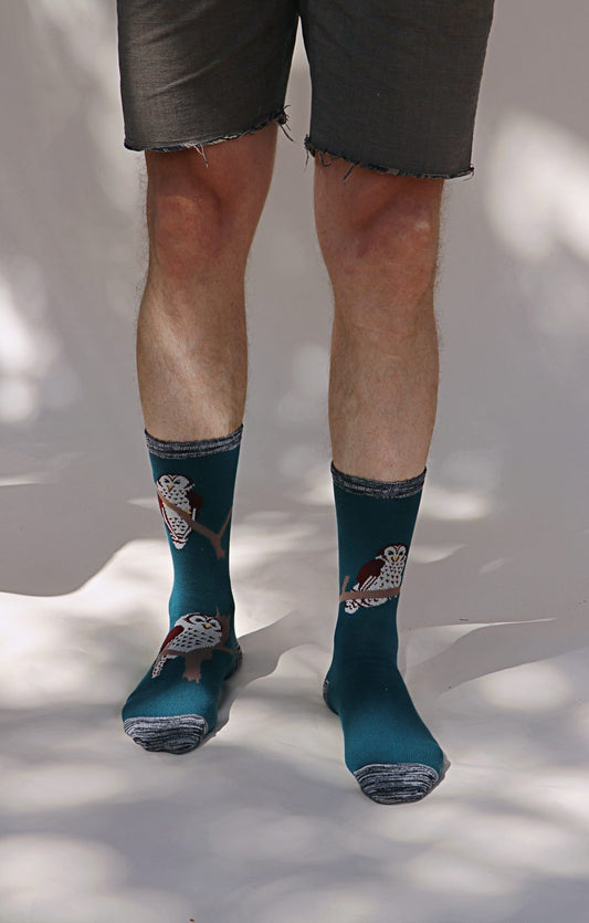 Male leg wearing TABBISOCKS brand Replant Pairs Owl Socks in green Spruce color with an overall design of an illustration of an owl, with gray point color at the toe and mouth of the sock