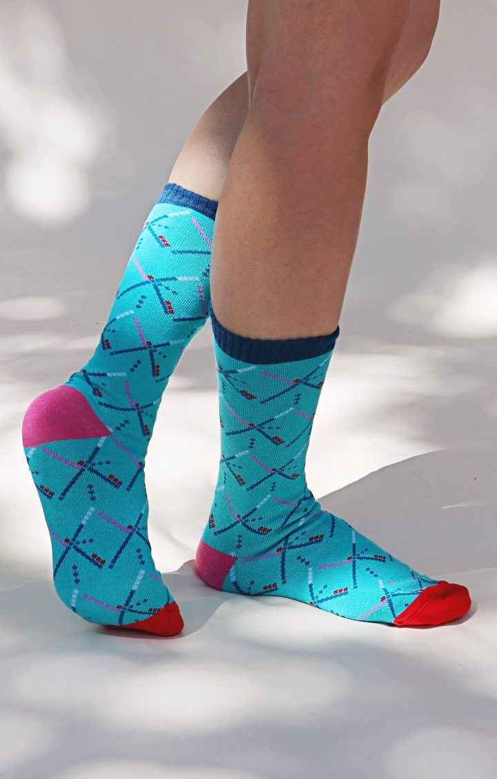 Light blue of TABBISOCKS brand Replant Pairs PDX Carpet Socks, male leg wearing socks with PDX Carpet design all over, with red toe, navy blue footwear and pink point color at the heel