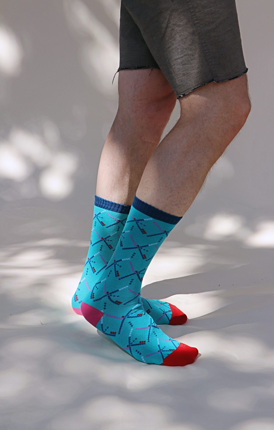 Light blue of TABBISOCKS brand Replant Pairs PDX Carpet Socks, male leg wearing half pants wearing socks with PDX Carpet design all over, red toe and dark blue footwear, pink point color at heel