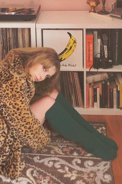 A woman in a tiger-striped jacket wearing a dark green Spruce color of TABBISOCKS brand Scrunchy Over the Knee Socks knee-length knee socks is relaxing in her living room