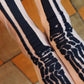 TABBISOCKS brand Sheer Skeleton Socks in the color white transparent fabric with black bone prints on the socks, female foot in Halloween costume.