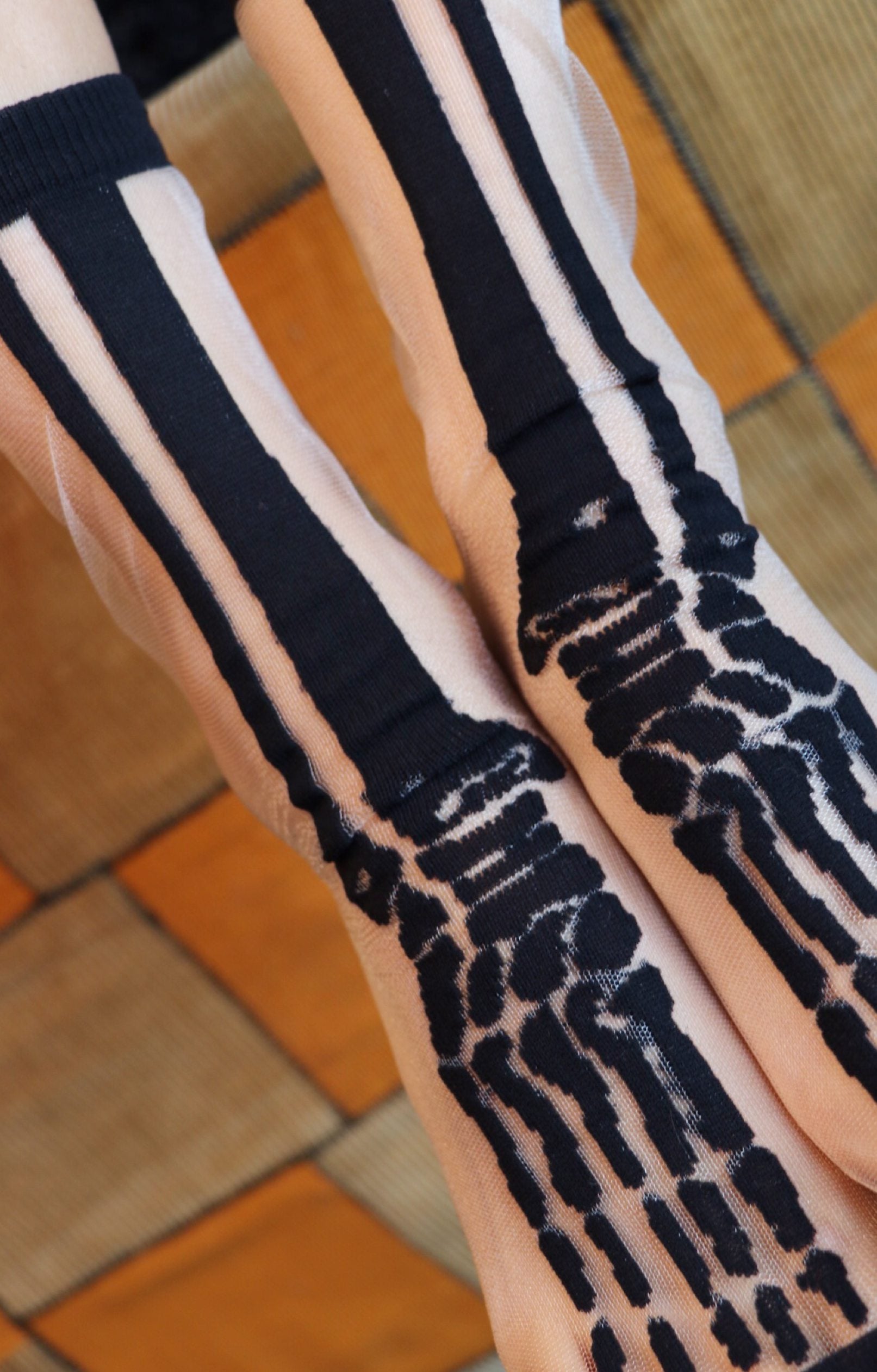 TABBISOCKS brand Sheer Skeleton Socks in the color white transparent fabric with black bone prints on the socks, female foot in Halloween costume.
