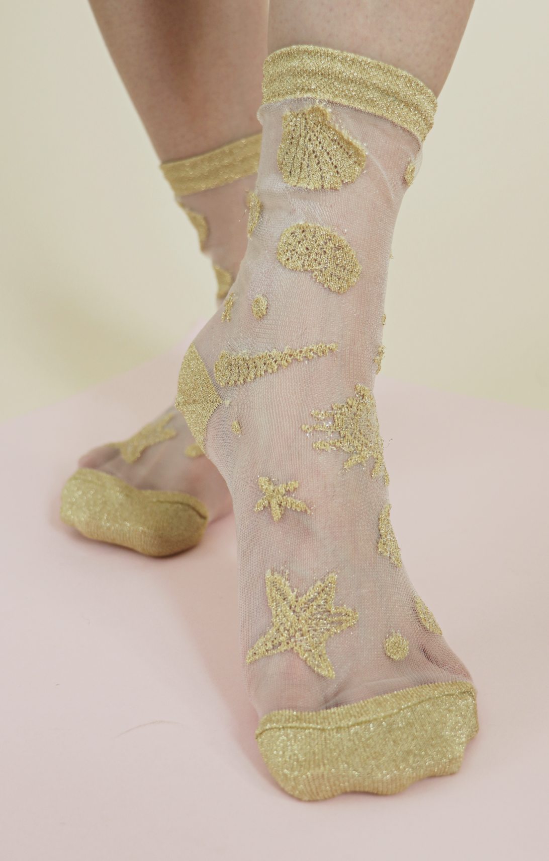 TABBISOCKS brand Shimmery Clear Seashell Socks in CLEAR GOLD color with gold-colored seashell and starfish embroidery scattered on transparent white fabric.