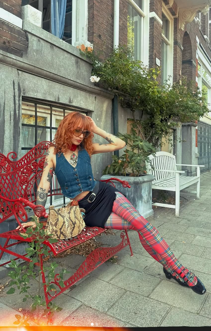 Woman sitting on a red bench in an urban setting with a building and plants in the background.