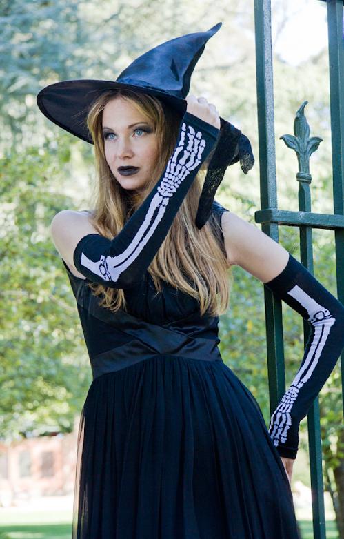 Woman in a witch Halloween costume wearing TABBISOCKS brand Skeleton Arm Warmers Long with white bone print on black fabric.