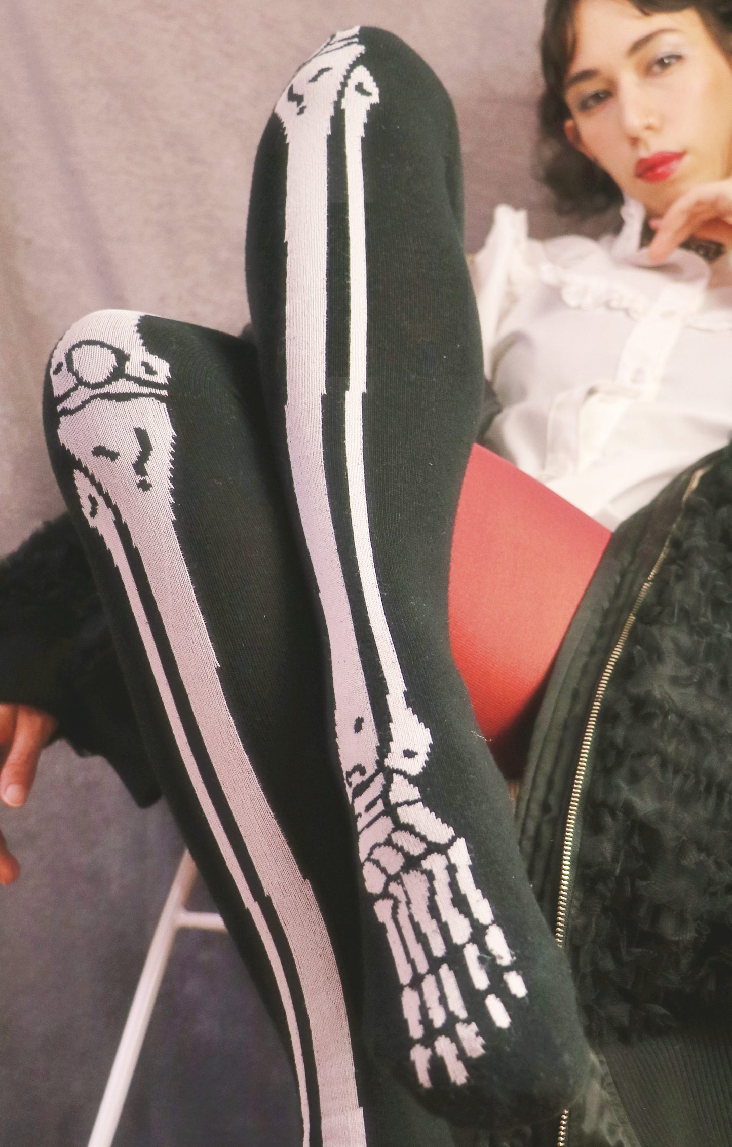 Skeleton Over The Knee Socks by TABBISOCKS brand, a woman in a sitting Halloween costume wearing a product that is entirely black in color with a white bone print.