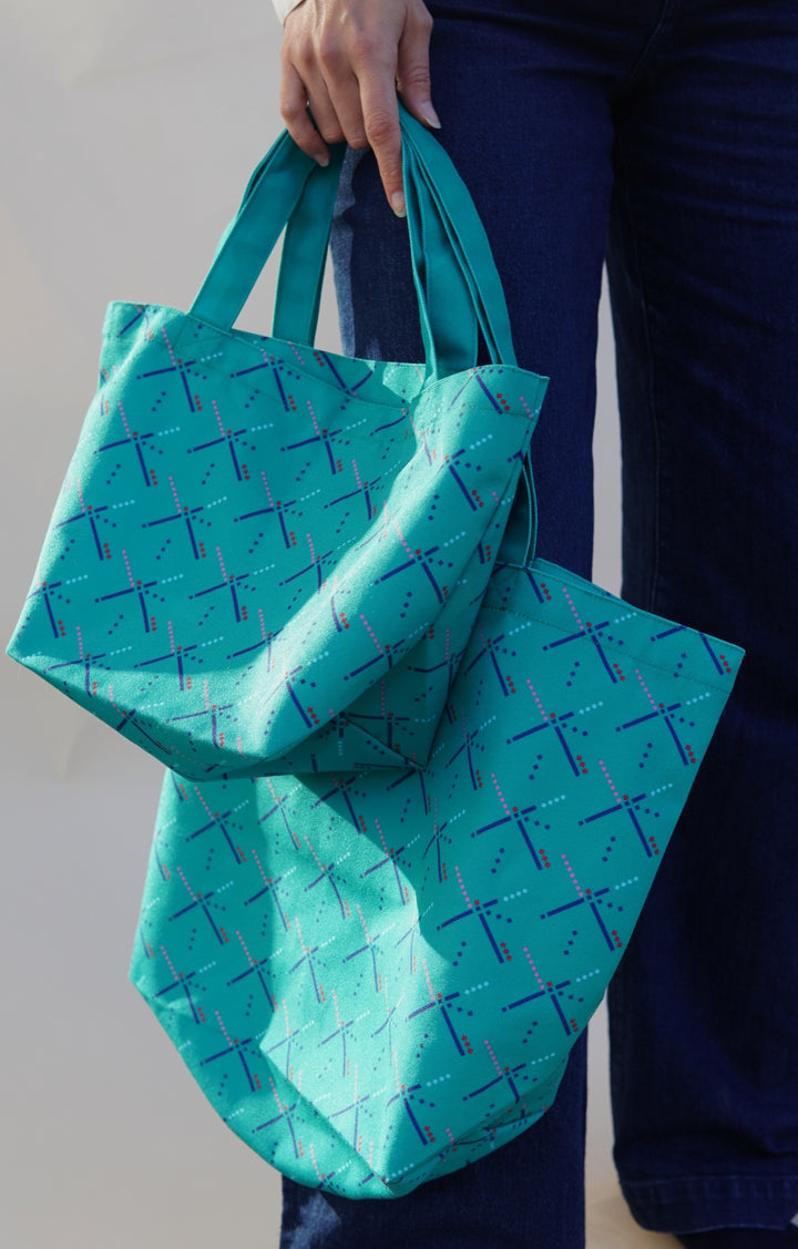 Person holding two turquoise reusable bags with a pattern against a neutral background