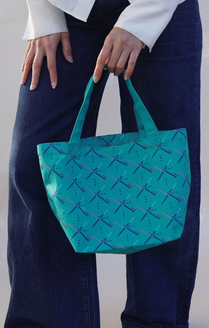 Person holding a teal tote bag with blue patterns against a neutral background