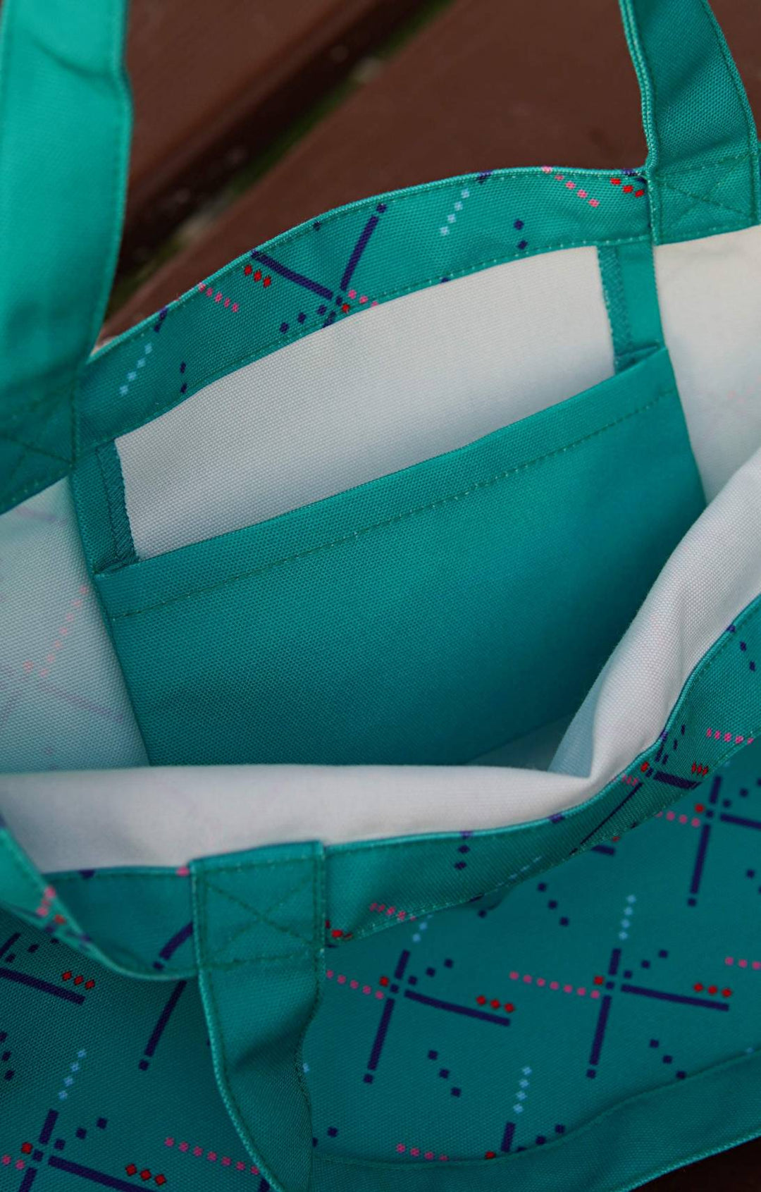 Teal tote bag with white interior and blue geometric pattern on a wooden surface