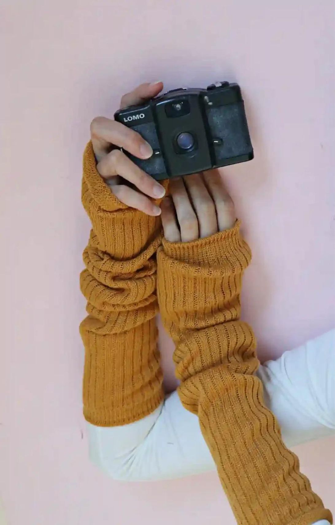 Arm of a woman holding a camera wearing a white cut and sewn shirt in the Mustard color of TABBISOCKS brand Wool Blend Leg and Arm Warmers
