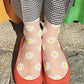 Leg of a woman wearing white and black gingham check pants with orange pumps wearing socks in CLEAR WHITE color of a product called Daisy Sheer Socks of the TABBISOCKS brand with white daisy flowers illustrated throughout on a transparent white fabric