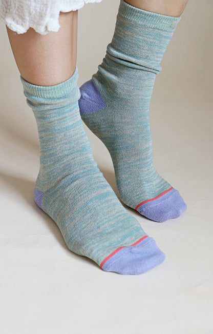 A woman's leg wearing a pair of TABBISOCKS brand Heather Organic Cotton socks in DUSTY MINT color with blue toes and heels and red lines as the point color.