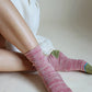 Legs of a woman in white loungewear wearing socks of TABBISOCKS brand Heather Organic Cotton in ROSE PINK color with green toes and heels and light blue lines as point colors