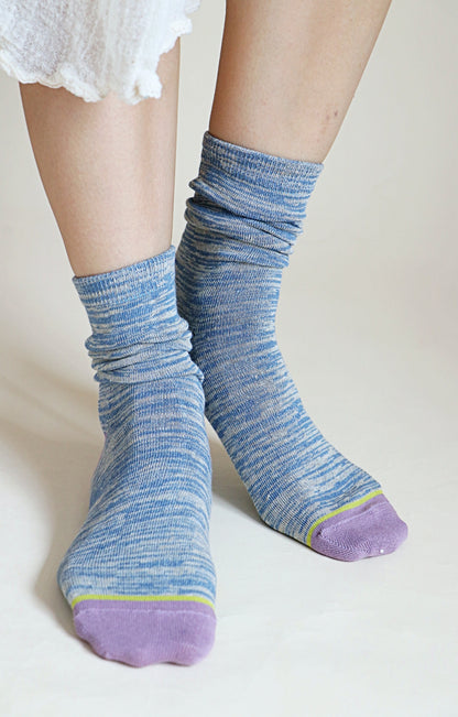 A woman's leg wearing a pair of TABBISOCKS brand Heather Organic Cotton socks in STEEL BLUE color with purple toes and heels and a yellow-green line as the point color.