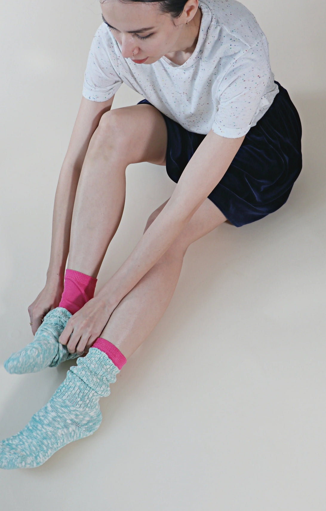 Woman sitting and double wearing the pink color of TABBISOCKS brand Washable 100% Finest Silk Toe Liner Socks with light blue socks