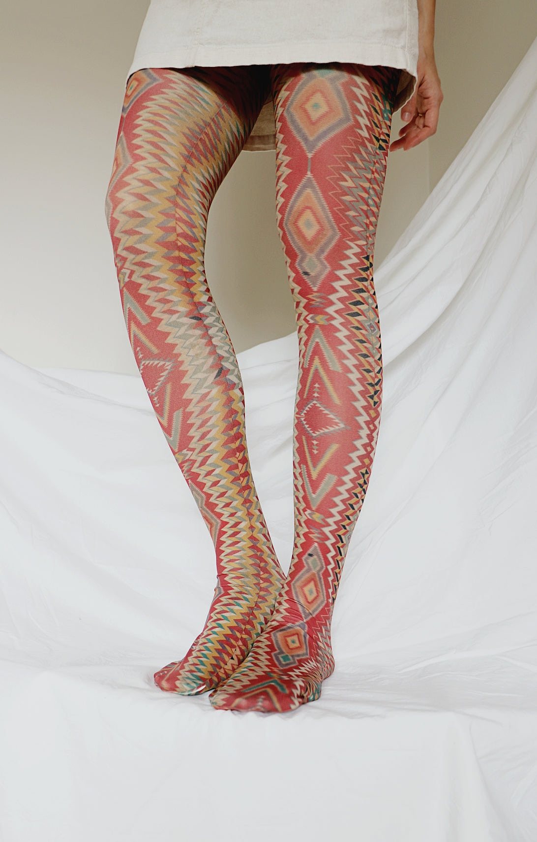 TABBISOCKS brand Germantown Eyedazzler Tights, women's legs wearing tights with an overall orange, geometric pattern.