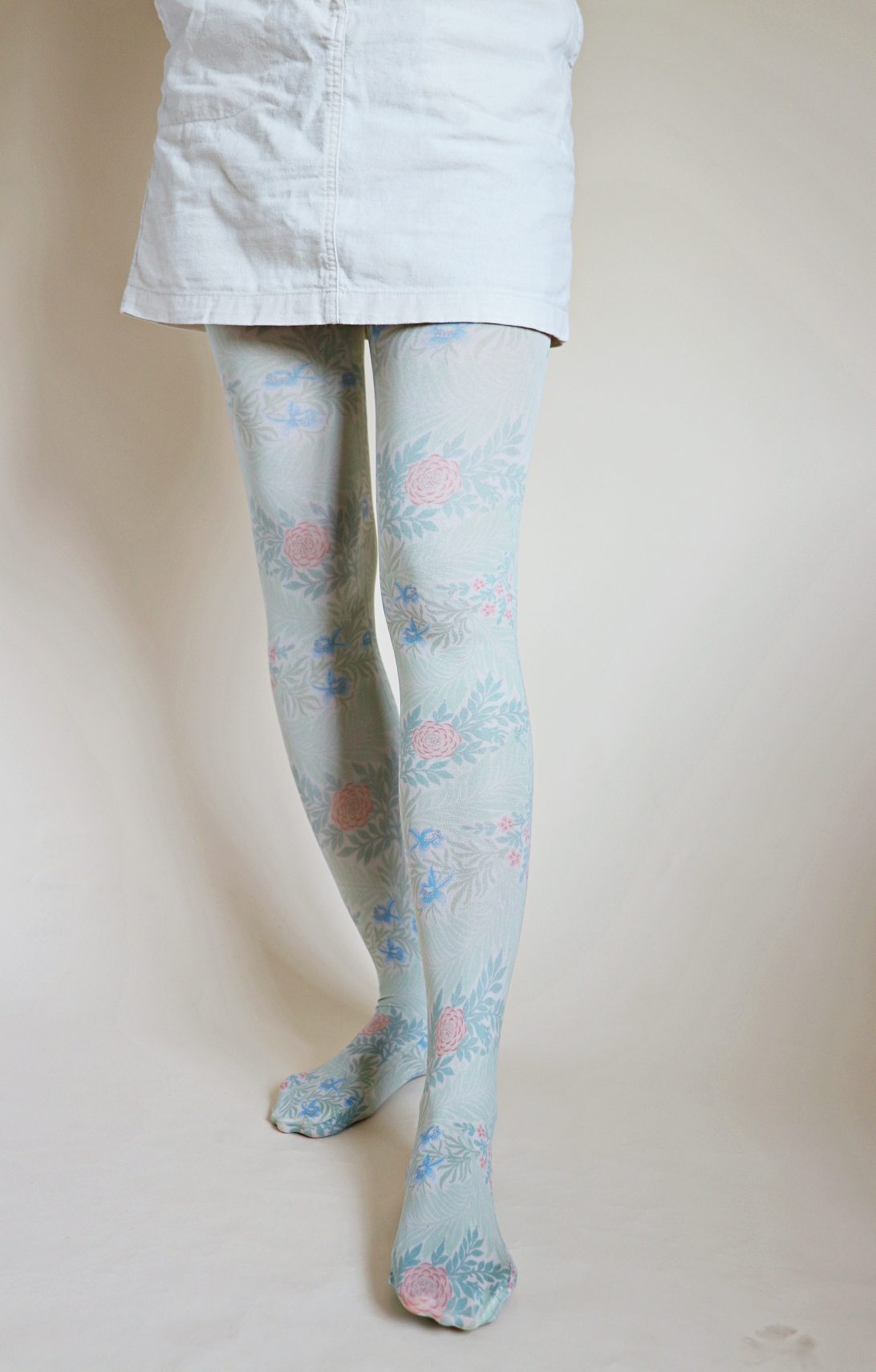Tights called Larkspur from the William Morris collection of the TABBISOCKS brand, with an overall design of illustrated pink flowers in an antique-ish light blue color